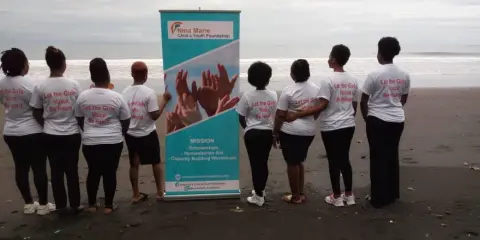 Volunteers in matching t-shirts standing in a line on a beach beside a foundation banner