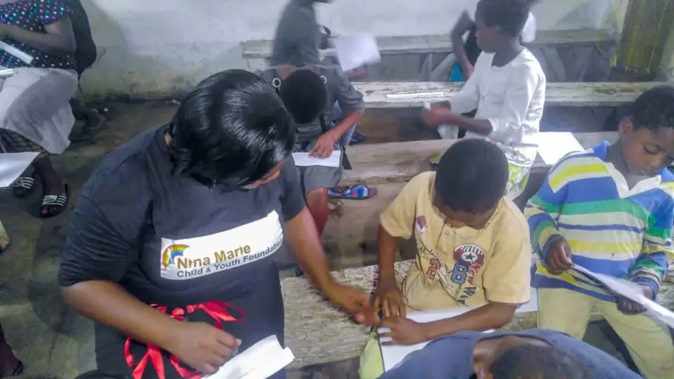 A volunteer leaning over a desk to help a young child with their schoolwork