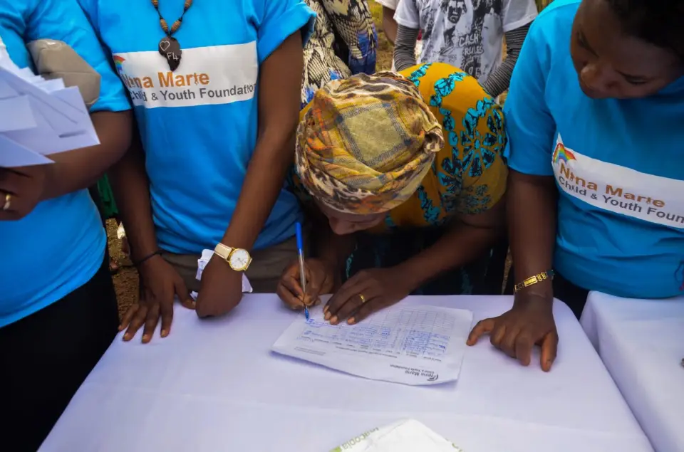 Volunteers in foundation t-shirts gathered around a table as a woman signs a register
