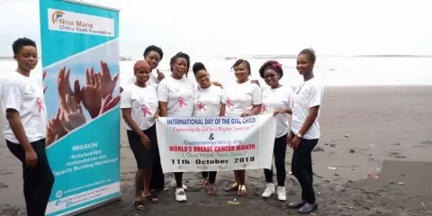 A group of volunteers on a beach holding a banner for the International Day of the Girl Child