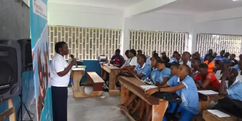 A speaker addressing a classroom full of secondary school students in blue uniforms