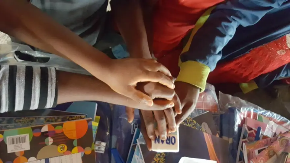 Several hands reaching together over a pile of school supplies