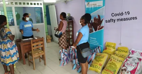 Volunteers distributing bags of rice and supplies beside a Covid-19 safety measures banner