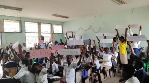 A classroom of students holding up handwritten signs during a talk on gender-based violence
