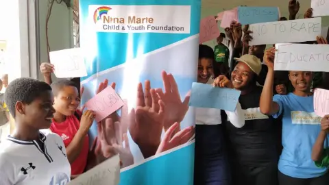 Students standing in front of a foundation banner holding signs about ending violence and rape
